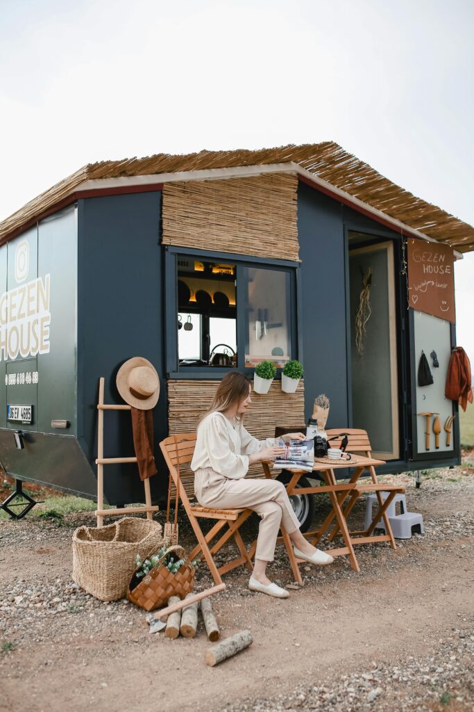 Woman relaxing with a magazine outside a stylish mobile tiny house, enjoying the serenity of nature.