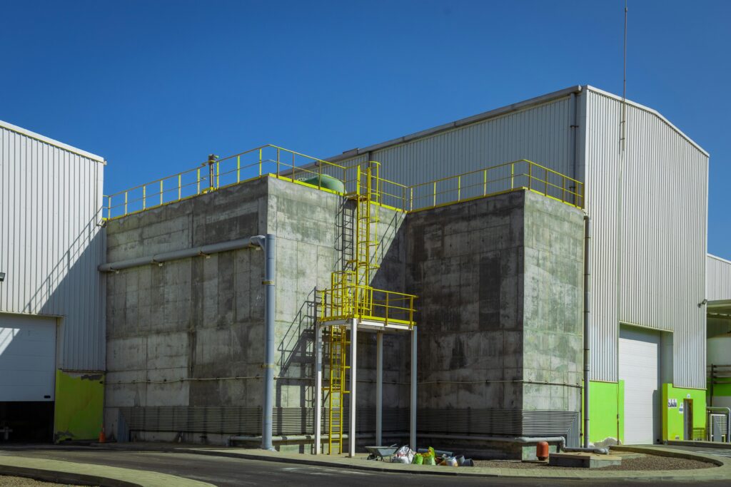 Modern industrial warehouse exterior with concrete facade and yellow railings under clear blue sky.