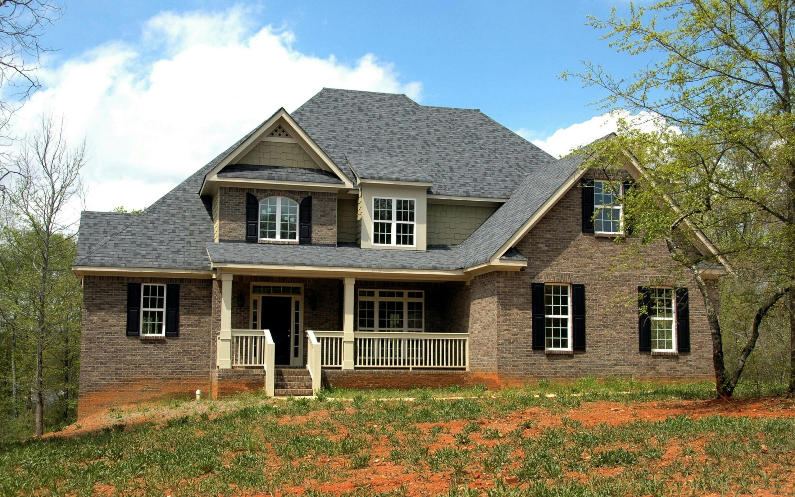 Classic two-story brick house with gable roof and front lawn in suburban setting.