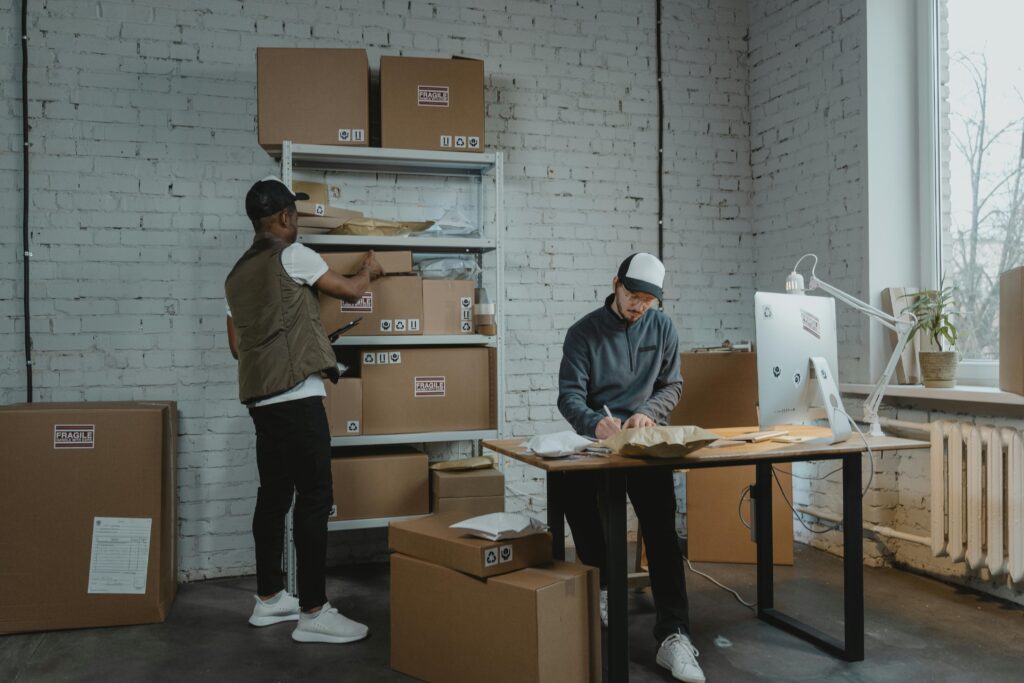 Two workers handling packages and organizing stock in a warehouse setting.