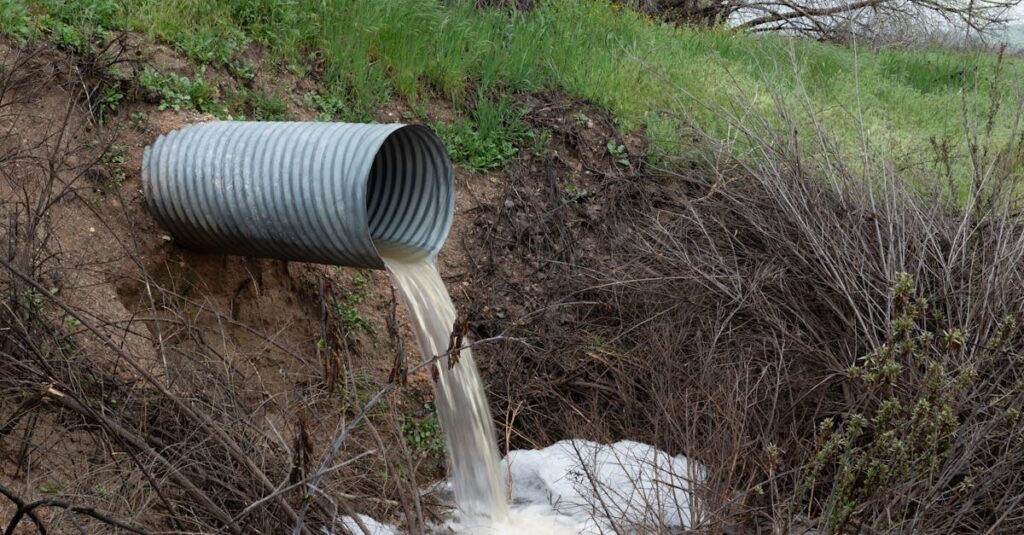A rural drainage pipe pouring water into a natural ravine, surrounded by green vegetation.
